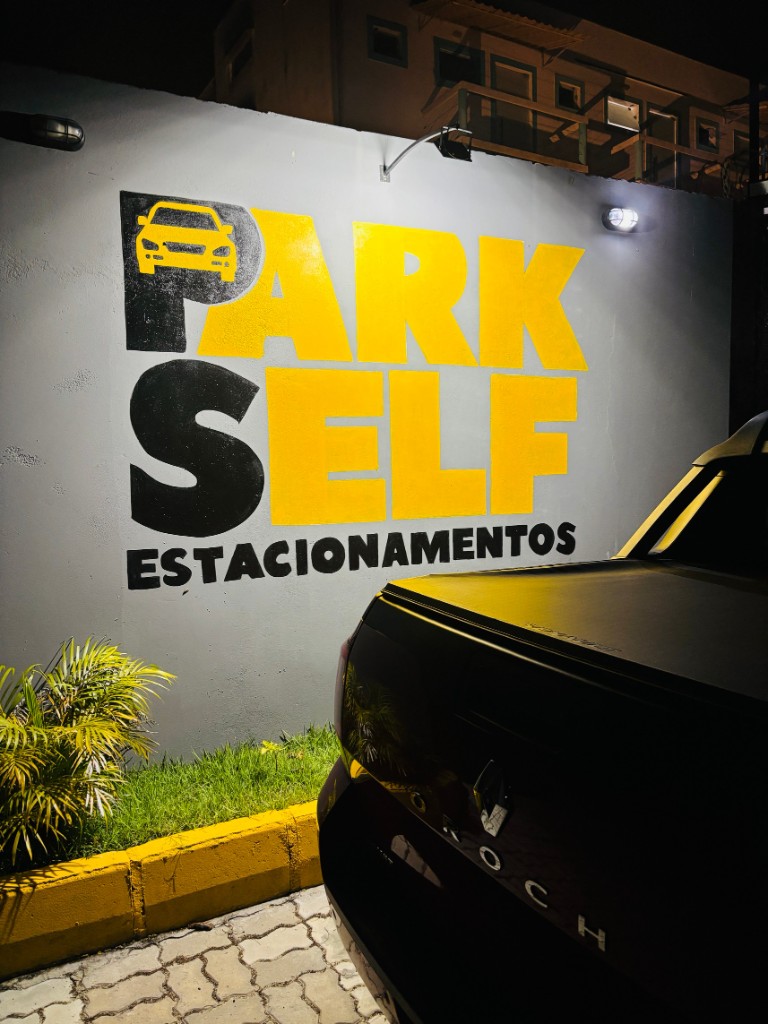 Fachada iluminada do Park Self Estacionamento à noite com logo amarelo em Porto Seguro